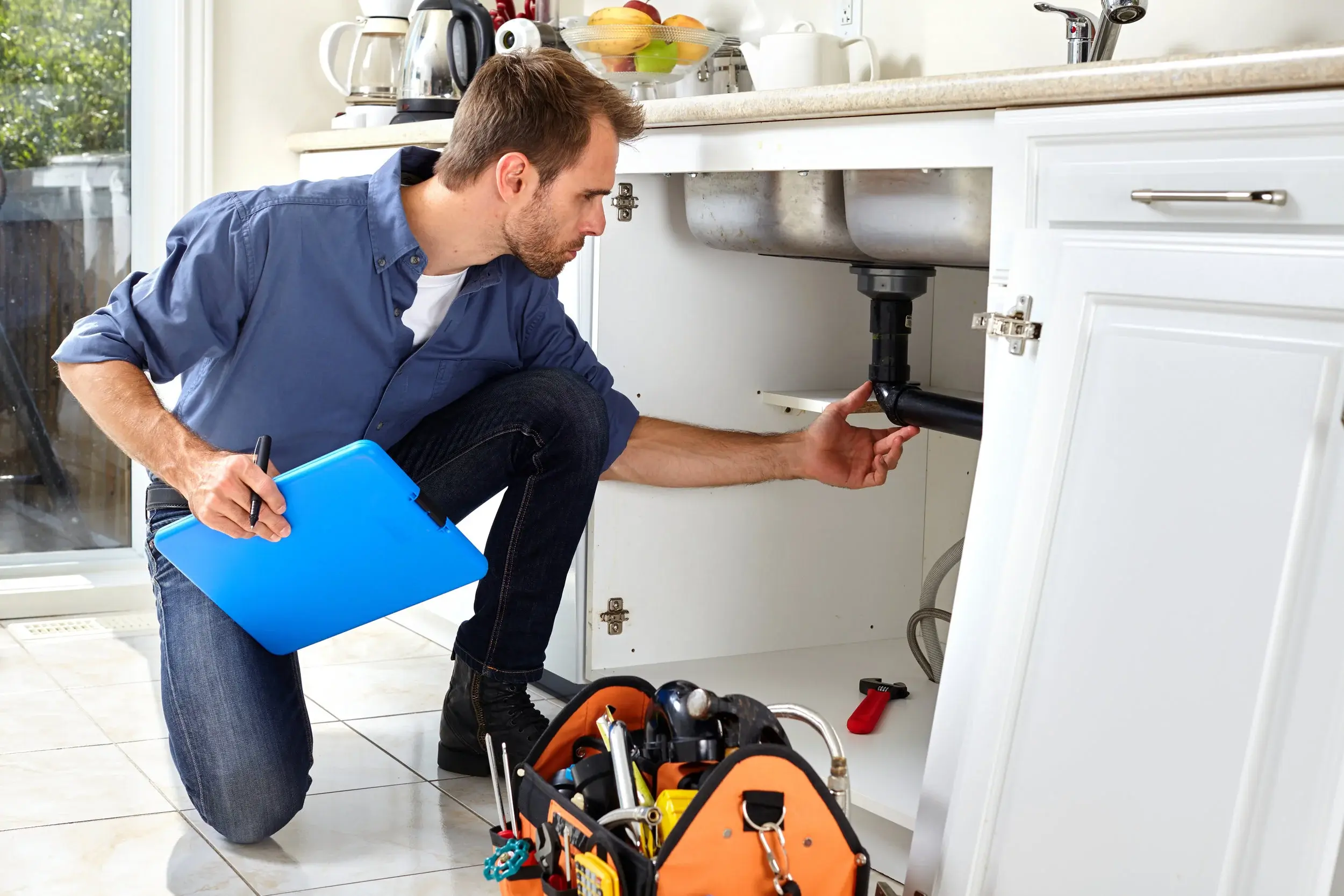 Professional plumber in Hertfordshire inspecting sink pipe drainage underneath a kitchen cabinet.