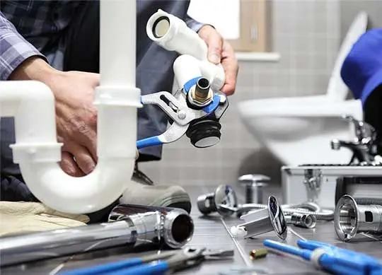 Professional plumber in Luton using pliers to assemble plastic and copper sink drainage pipes in a bathroom.